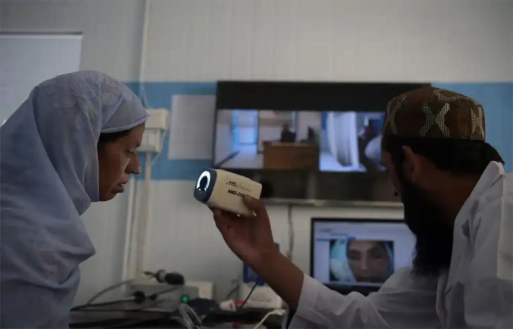 Man scanning woman’s face at computer desk and Healthcare in Rural Pakistan